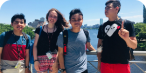 four young cogito high school students smile for a group photo in front of the charles river in the city of boston